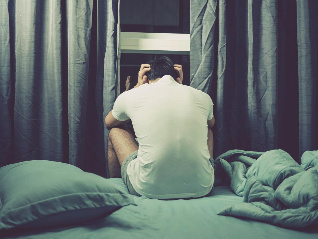 Man sat on the edge of bed with his head in hands due to orgasm headache