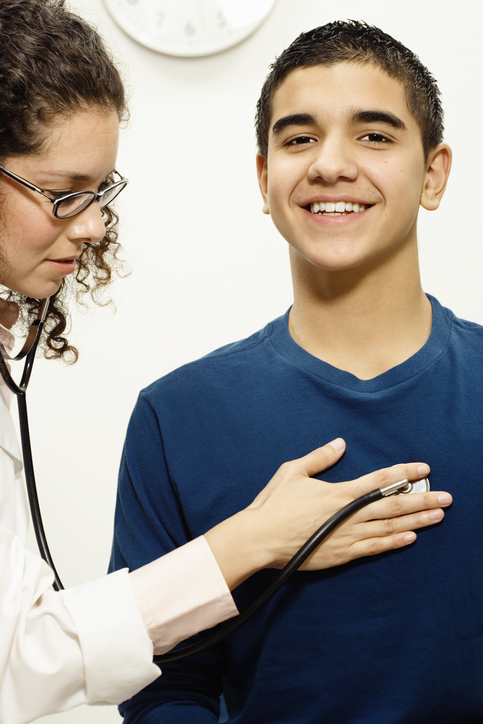 Female doctor checking male teen patient with stethoscope
